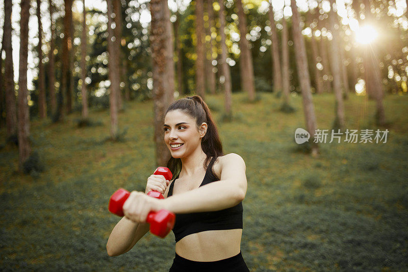 一个漂亮的女人在锻炼的时候用了哑铃。女人伸展和锻炼与重量户外