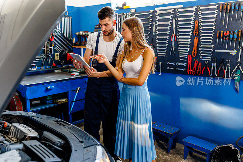 一位汽车修理工正在用平板电脑向一位女顾客解释汽车的问题。