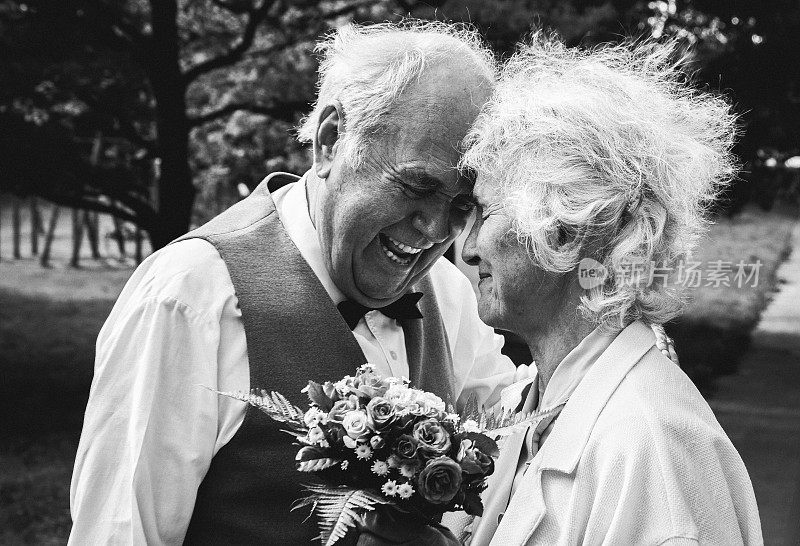 一对老夫妇在绿色的公园里散步。祖母和祖父在他们的金婚纪念日上。50年的爱情故事。奶奶和爷爷在接吻。黑色和白色。