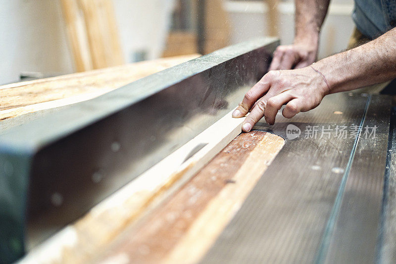 木匠在木工车间用手把一根木棒装进机器里。