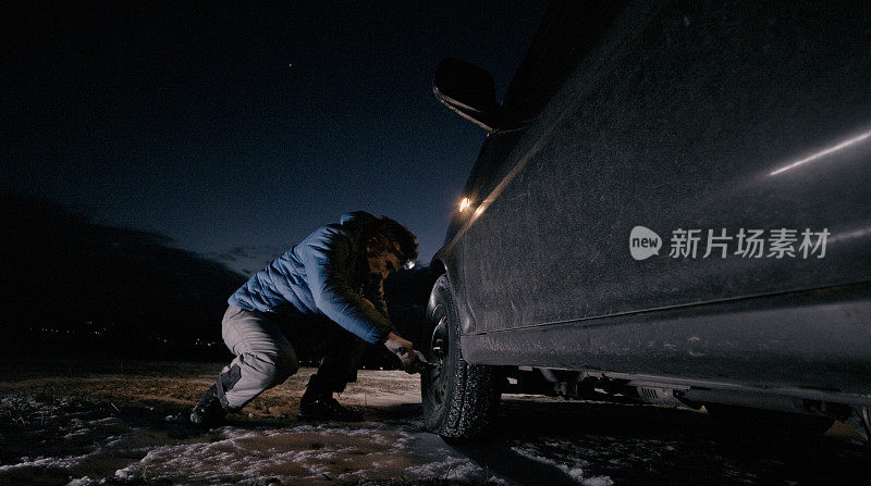 在冬天的路上，一名男子在晚上给汽车换轮胎。