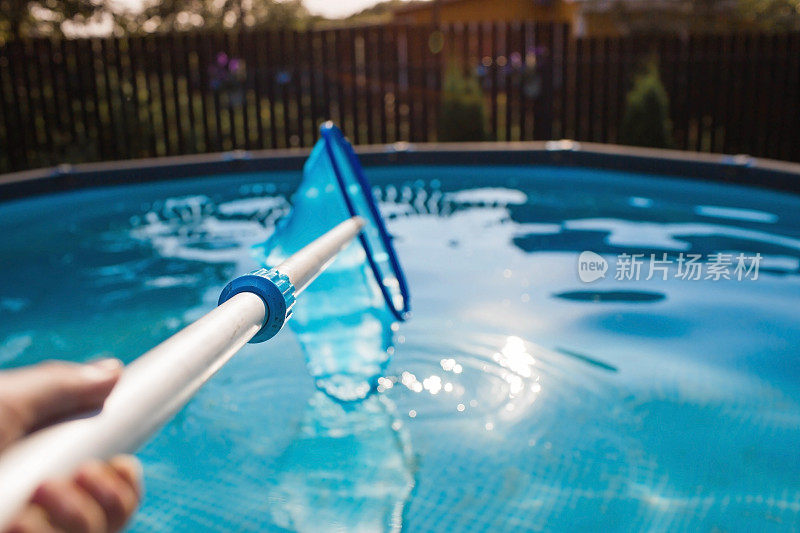 用带网眼的金属框架清理游泳池的污垢。操作期间的池清洁剂。太阳能旗帜。暑假的概念。抽象模糊和散焦背景。