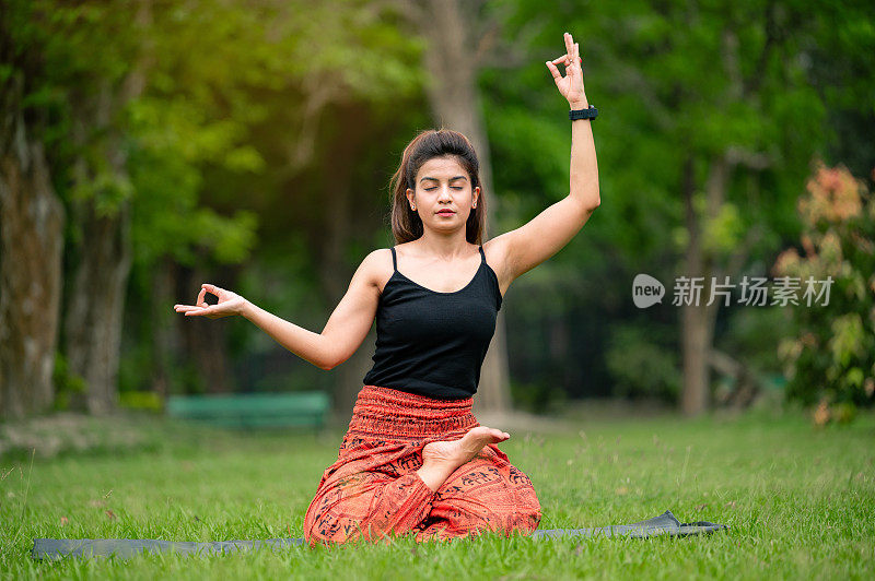 快乐的年轻女子做瑜伽伸展手和在公园室外冥想。