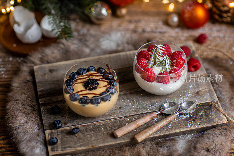 圣诞甜点crème焦糖和意式奶冻与新鲜浆果在乡村木厨房和圣诞灯