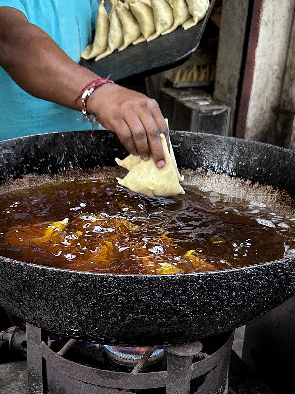 特写镜头:无法辨认的人将萨莫萨放入卡拉希(印度锅)，冒泡的热油，油炸的萨莫萨，印度街头小吃摊，不健康的饮食，聚焦于前景