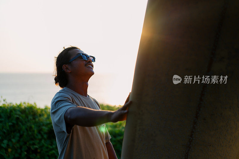 夕阳下，印尼男冲浪者看着他的冲浪板