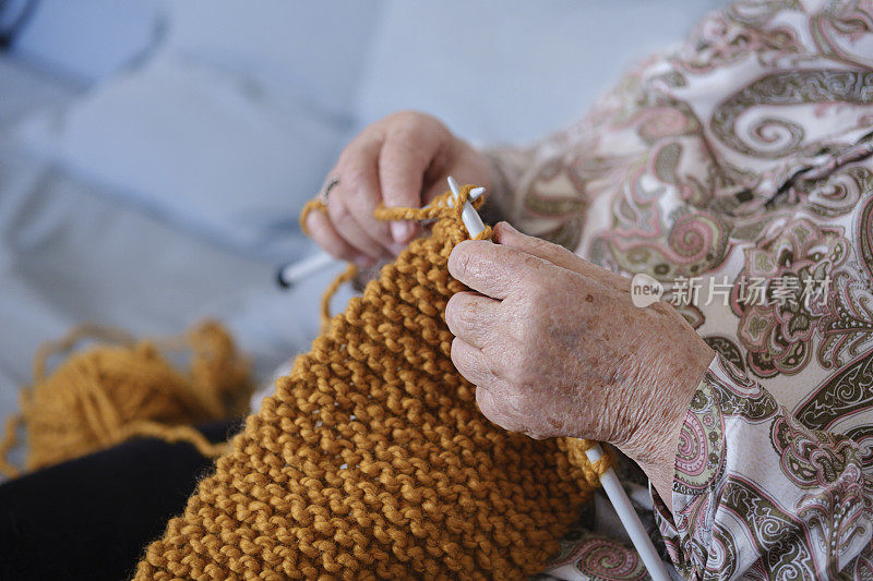 照片中，一位老妇人正在织毛衣，脸是看不见的