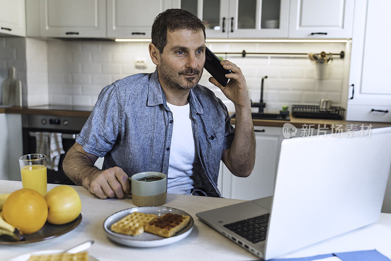 一名男子早上在厨房餐桌边吃早餐时使用笔记本电脑。