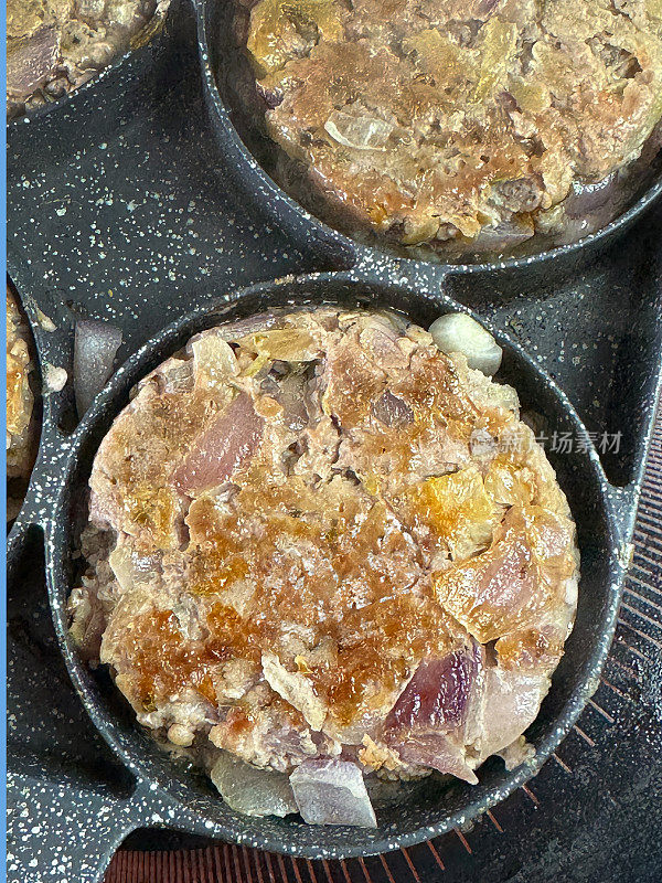 一个不粘锅的全画幅图像，包含四个金属环，里面装满了棕色的香肠肉和红洋葱汉堡肉饼，在陶瓷滚刀上的锅里煮，升高的视图