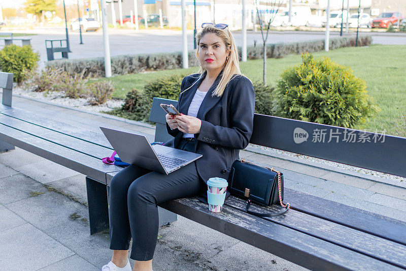 女人一边使用科技，一边享受城市的绿色空间。在户外灵活工作。现代虚拟理财咨询。