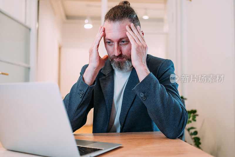 压力大的商人在办公室用笔记本电脑工作时头痛。