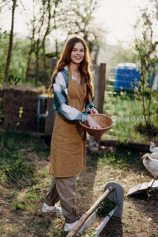 一名年轻女子在农场工作，她从碗里倒出新鲜的饲料喂鸡，并确保食物是干净和有机的，以保证脸和鸡的健康