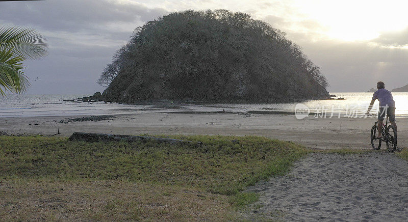 早上，一名男子骑着山地车沿着沙滩往下走