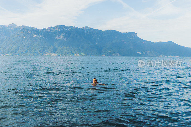 在美丽的日内瓦湖游泳的年轻人与风景优美的山脉在瑞士