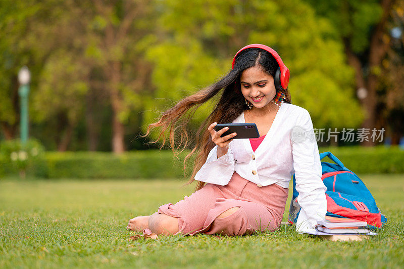 年轻女学生在校园公园用手机和耳机看视频