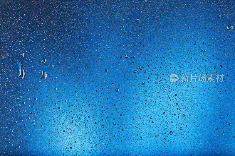 凝结或雨滴落在玻璃上。冰冷的磨砂玻璃，蓝色背景上有水滴