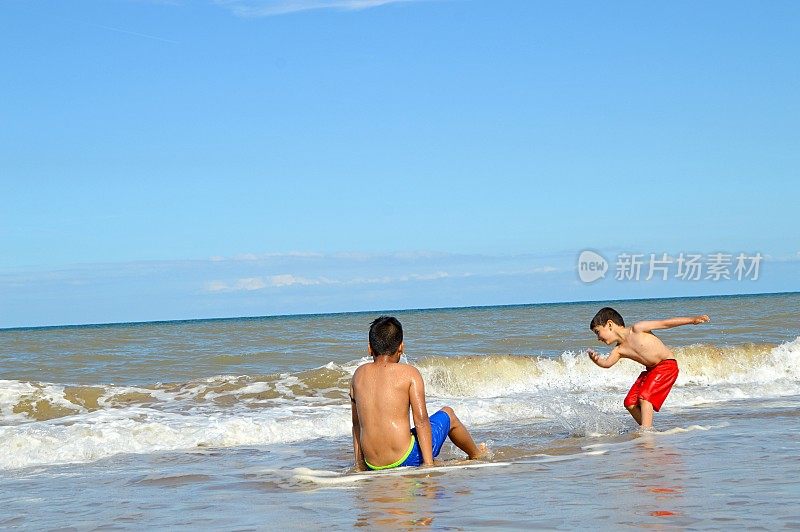 两个穿着蓝色和红色短裤的男孩在海滩上的海浪中玩耍