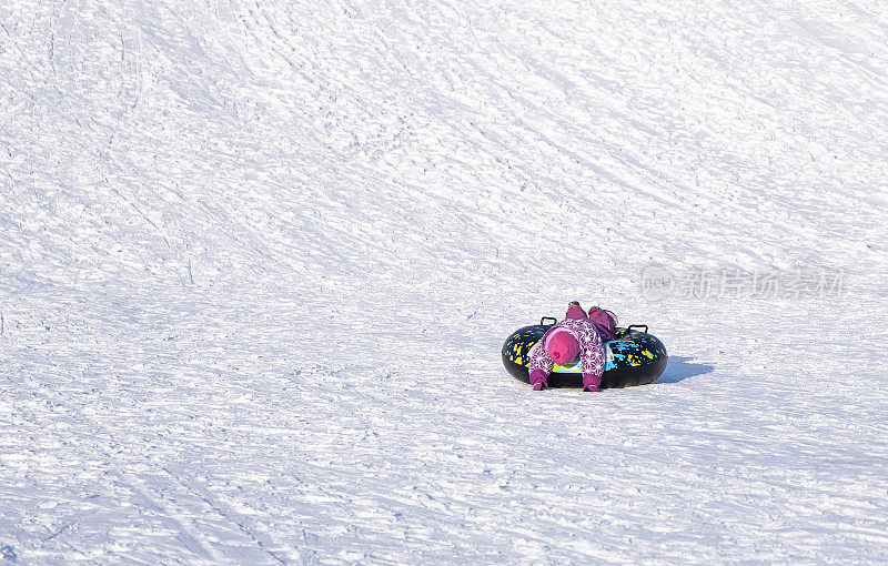 一个孩子，一个小女孩，厌倦了从积雪覆盖的滑梯上滚下来，躺在一个充气环上。冬季娱乐。