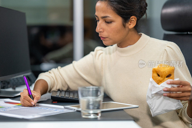 一名印度妇女一边在办公桌前工作，一边吃着糕点