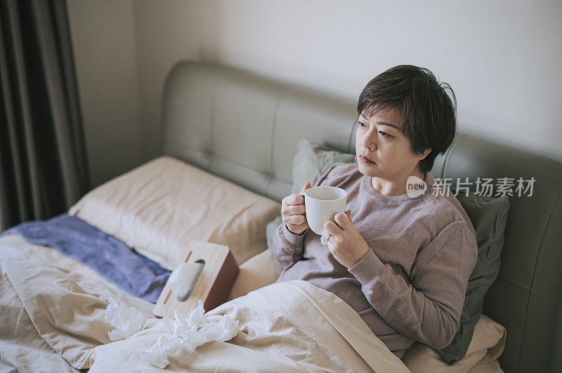 亚洲华人中年妇女喝热茶不舒服，生病在家卧室休息