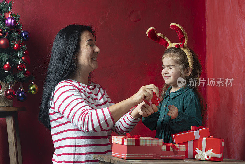 母亲和女儿与礼物盒和圣诞树摆姿势的照片