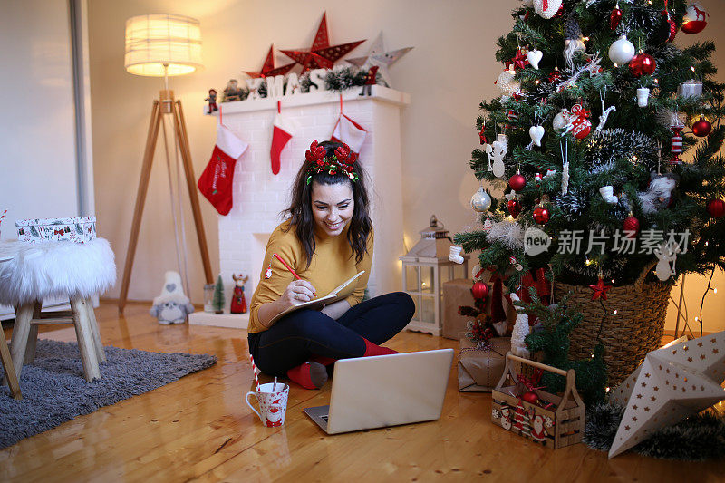 照片的快乐迷人可爱漂亮漂亮的女朋友坐在地板上看东西在笔记本电脑屏幕在新年前夕的照片