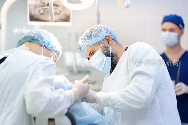 牙科手术中的外科医生和护士。手术室里被麻醉的病人。在诊所安装种植牙。