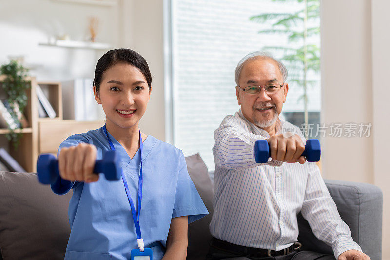 亚洲女性医生建议老年患者在家中使用哑铃进行锻炼。微笑的护士帮助老年病人锻炼肌肉。理疗师护理。