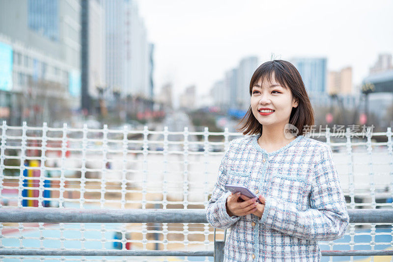 亚洲年轻女子手持智能手机站在城市街道上