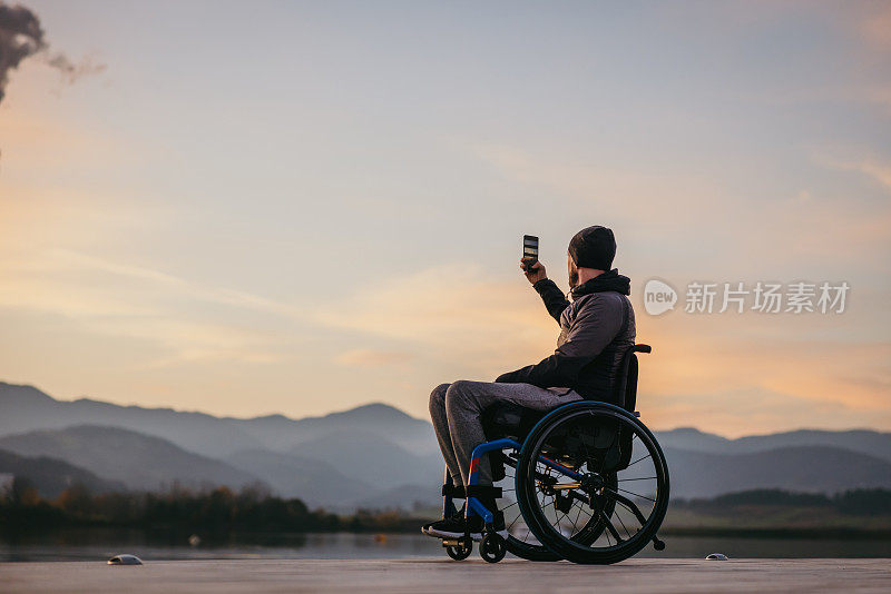 坐轮椅的残疾人在码头用手机拍照