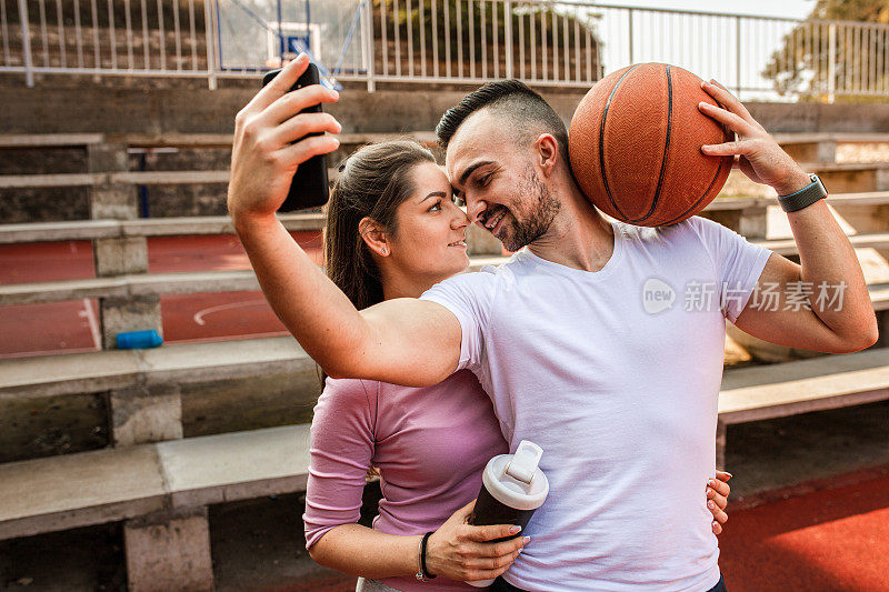 年轻情侣在街头球场打篮球时自拍