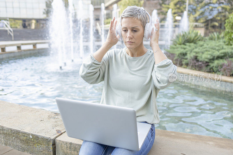 女士在户外使用笔记本电脑时戴上耳机