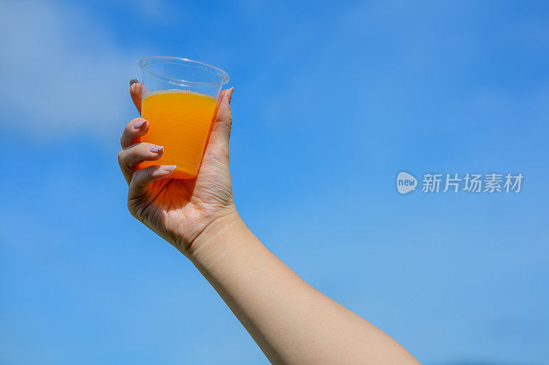 女人手拿橙汁在一次性塑料杯蓝色的天空