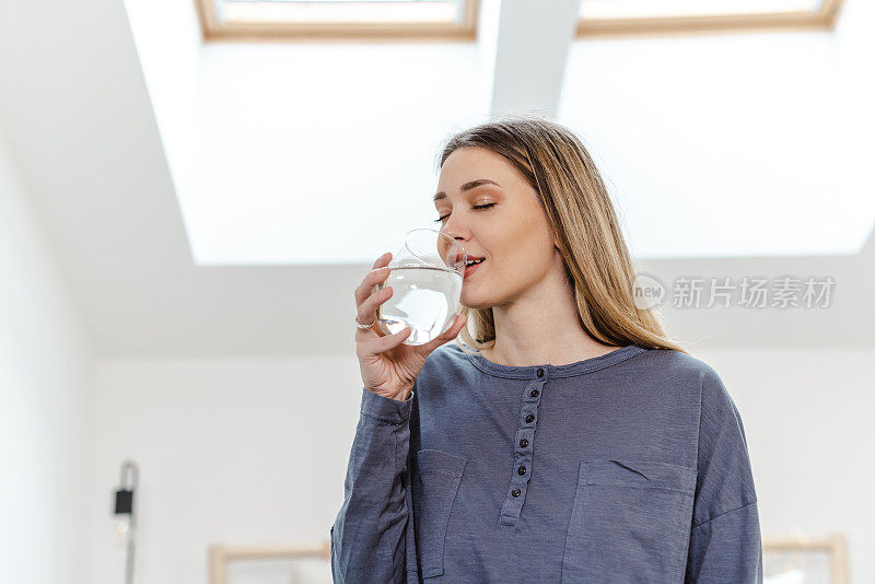 年轻女子在家里用玻璃杯喝水
