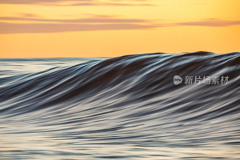 平滑的海浪在清晨形成金色的光和戏剧性的天空在日出