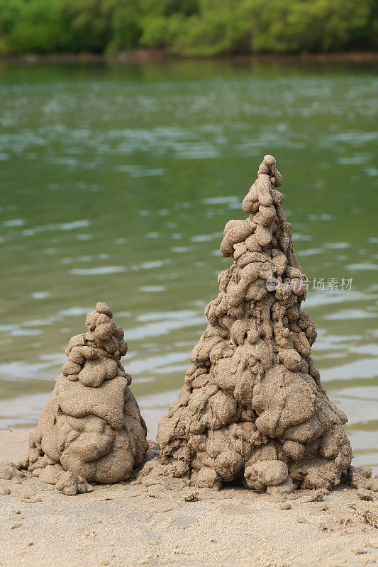 在低潮水的边缘的沙滩上滴沙城堡塔的特写图像，集中在前景