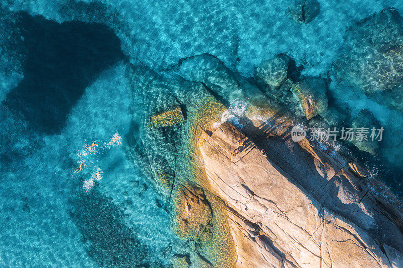 意大利撒丁岛，在蓝色的大海中游泳的人，岩石海滩，夏天日落时的海浪。热带的背景。景观。透明湛蓝的水和石头。顶部无人机视图。下视图