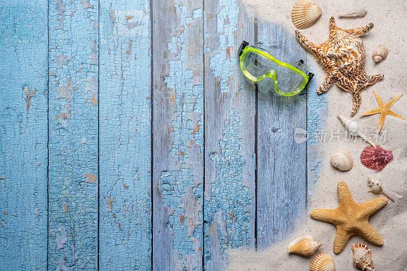 夏天，海滩和度假的概念与自由文本空间。前视图。平面布局，绿色潜水镜，大海星和海贝壳和各种海贝壳和细沙滩在一个古老的蓝色木板背景