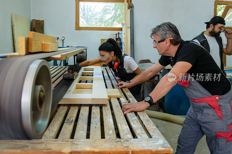 木工车间里，女木匠正在和男同事一起使用磨砂机。
