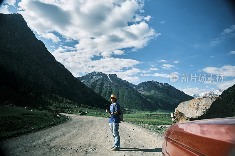 一位兴高采烈的女游客站在车旁边，正在拍摄她在天山自驾游的视频