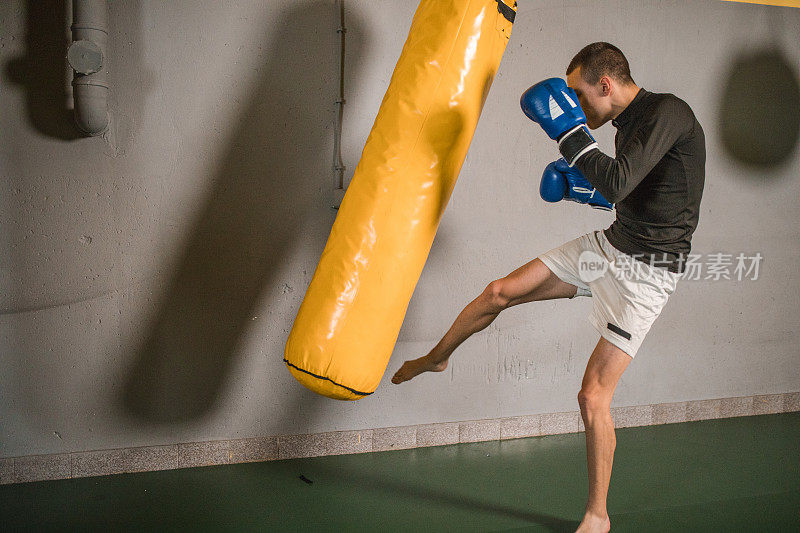 一个年轻强壮的自由搏击运动员在健身房击打沙袋，锻炼他的肌肉