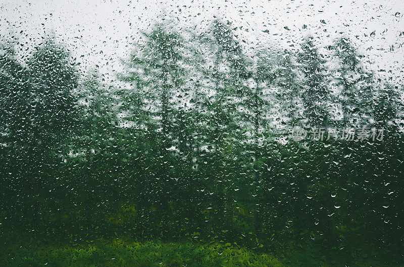 景观和多云的天空透过水滴雨潮湿的窗户
