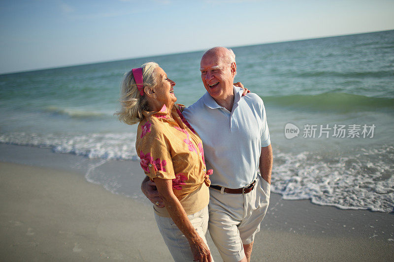 快乐的老夫妇在海滩边散步和欢笑