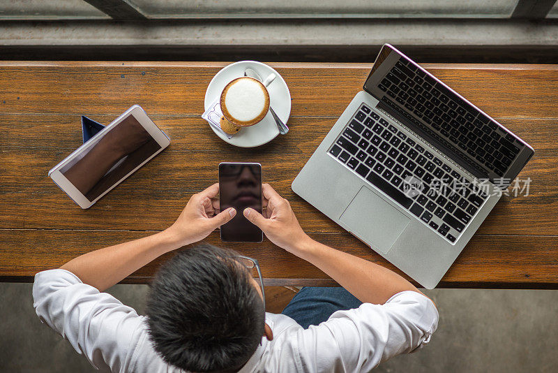 商人一边喝咖啡一边使用智能手机、平板电脑和笔记本电脑