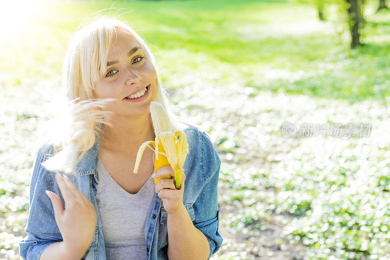 迷人的女人吃香蕉，自然的绿色春天的背景