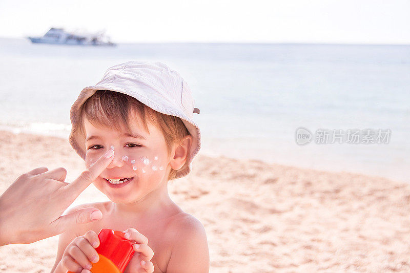 在海滩上给儿子涂防晒霜的母亲的手。