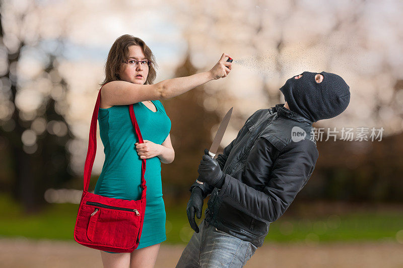 年轻女子正在用胡椒喷雾对抗持刀的持枪小偷。