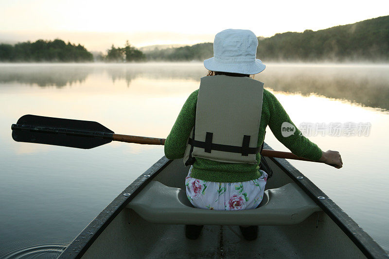 户外女孩在薄雾的晨湖上划着独木舟