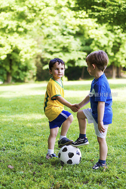 两个蹒跚学步的孩子在踢足球前握手