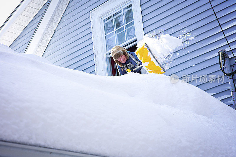 一个成熟的女人从屋顶上铲雪。